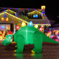 Green stegosaurus inflatable in a Santa hat with colorful lit back plates in front of a lit house