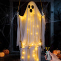 White draped ghost with fairy lights sitting on a rope swing with a remote in hand