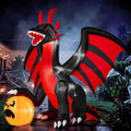 Black and red winged dragon inflatable opening its mouth beside a glowing jack-o'-lantern