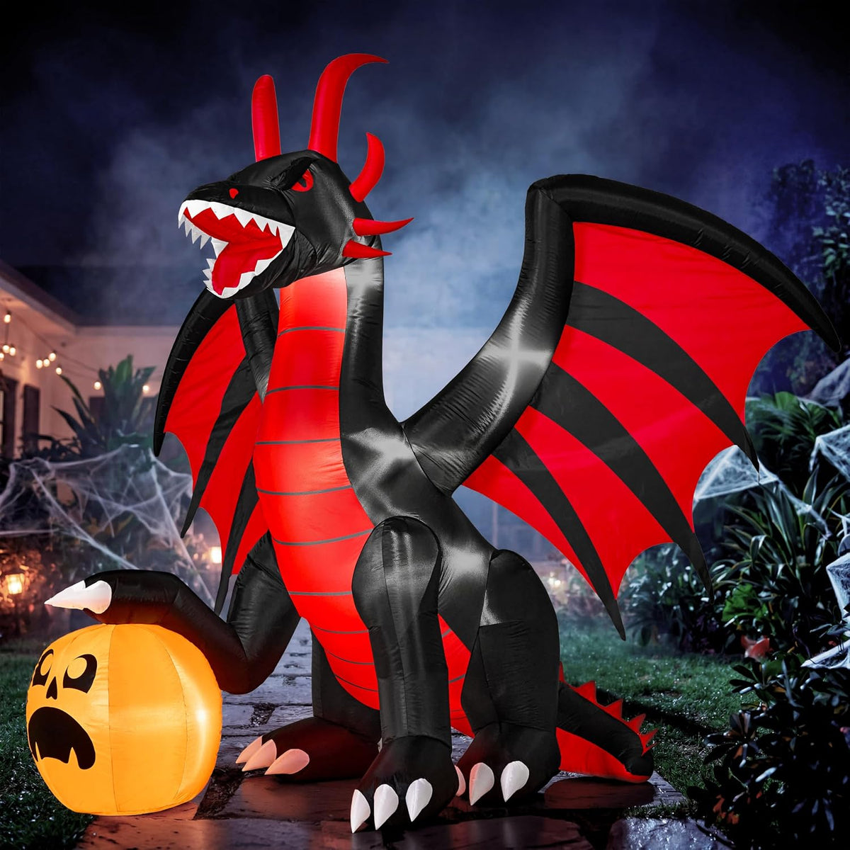 Black and red winged dragon inflatable opening its mouth beside a glowing jack-o'-lantern