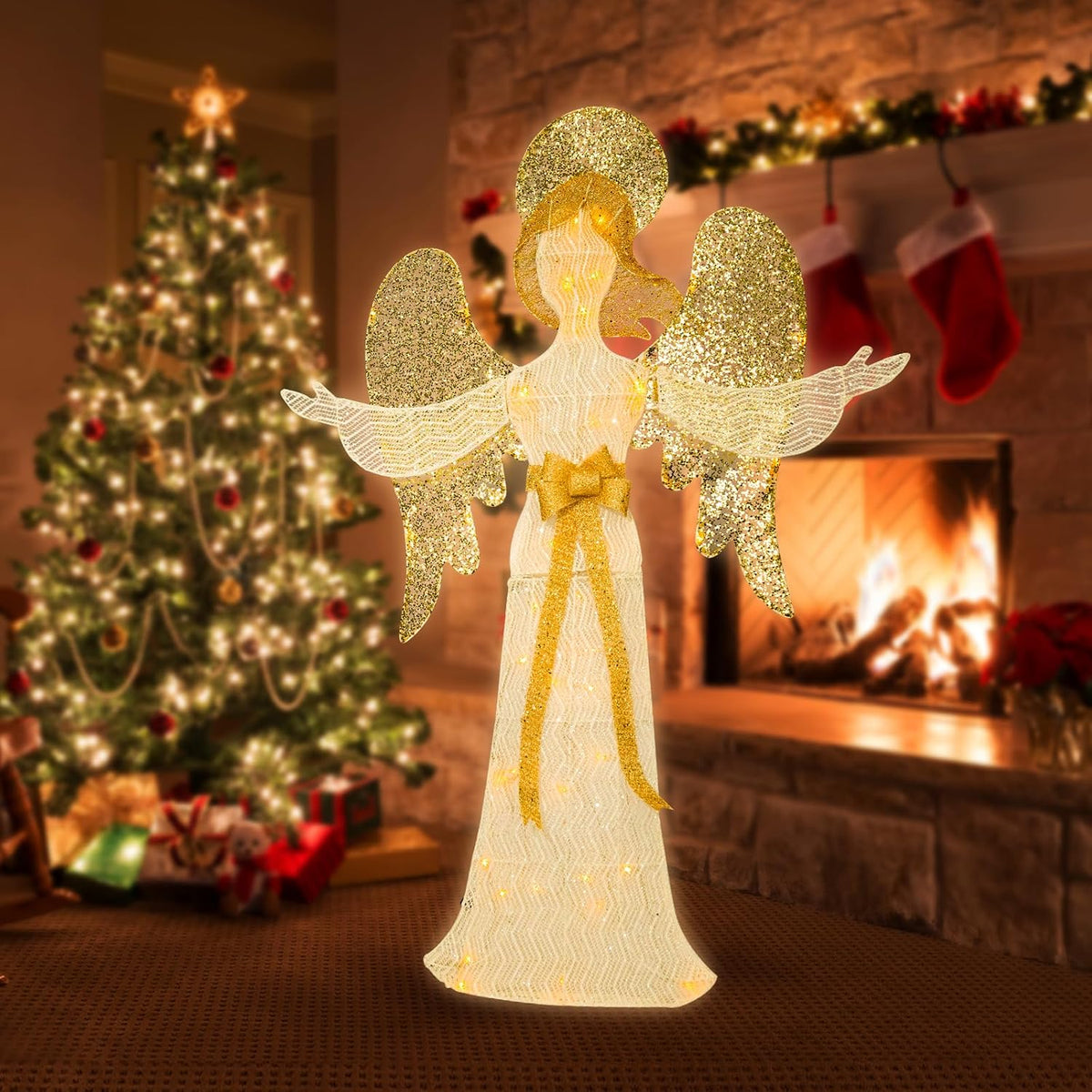 Lighted glittering angel in a white and gold gown with gold wings beside a Christmas tree and fireplace